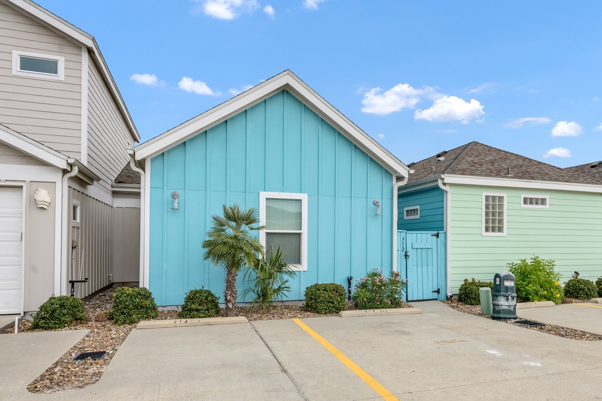 Charming coastal cottage features vibrant turquoise siding and tropical landscaping in a peaceful residential setting.
