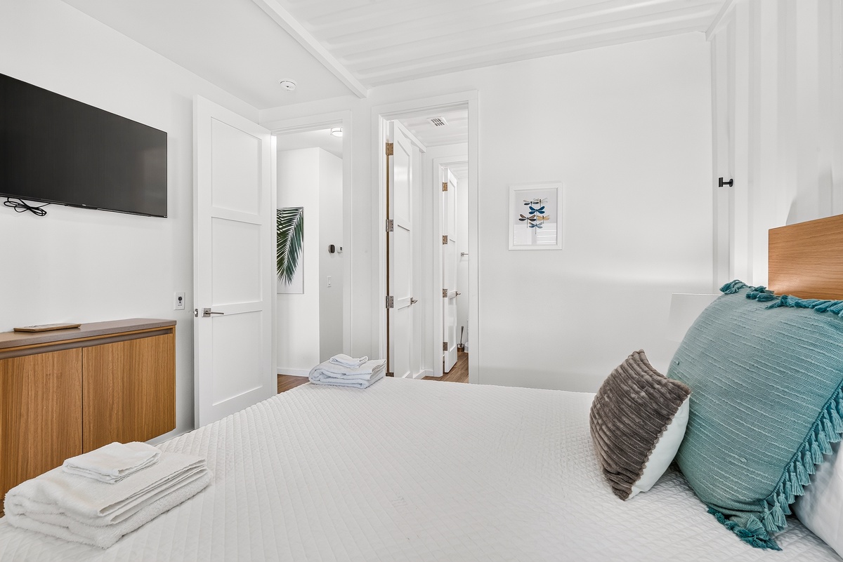Your bright, coastal-inspired second bedroom awaits with crisp queen linens, calming teal accents, and a private TV—a serene retreat for restful nights.