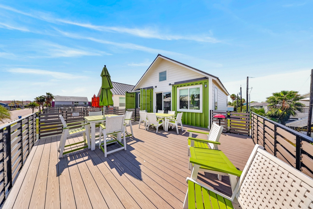 A bright rooftop deck overlooking the neighborhood, where multiple outdoor seating areas invite group gatherings under sunny skies and coastal breezes.