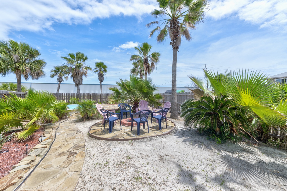 This coastal backyard features a circular patio with seating for gatherings, surrounded by tropical palms and beach views beyond the fence—a welcoming entrance to seaside relaxation.