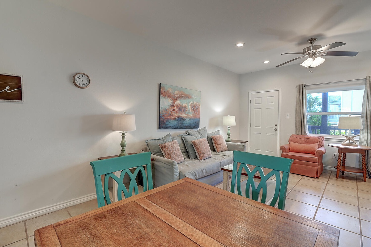 Relax in your bright, airy living space with comfortable seating, ceiling fan, and cheerful turquoise accents that create a welcoming coastal vibe.