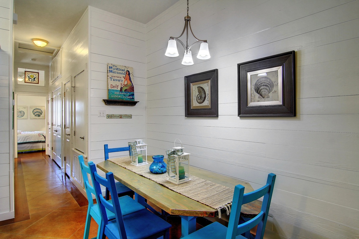 Gather around this charming dining table where coastal artwork and warm pendant lighting create the perfect atmosphere for your memorable meals together.