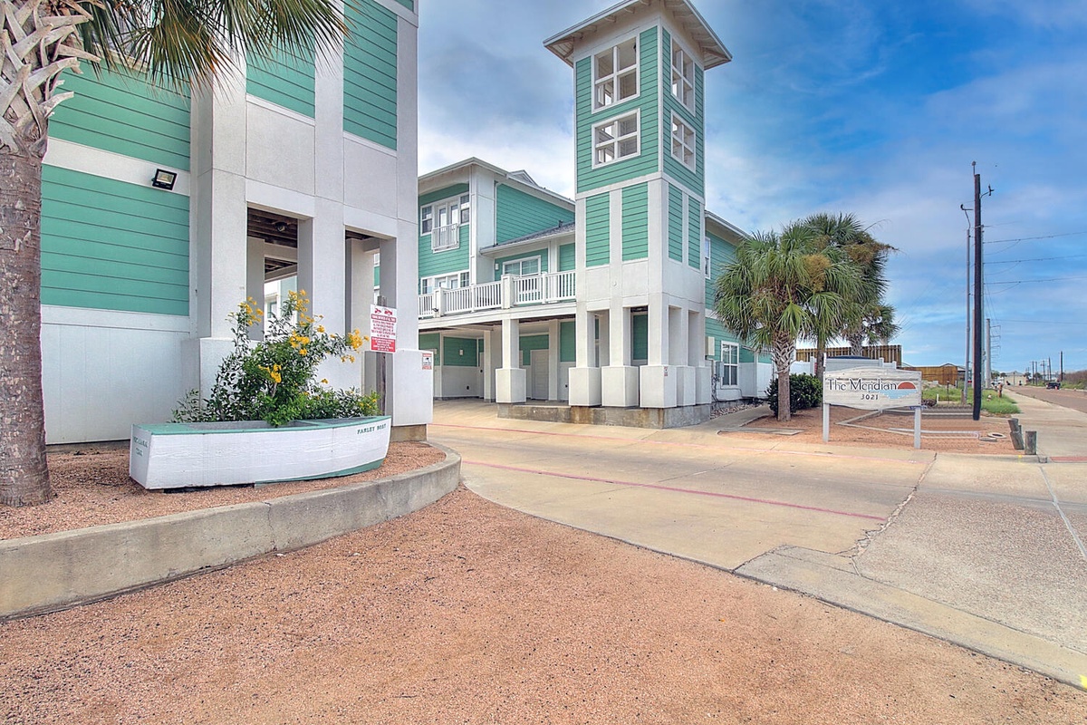 Coastal-style vacation property featuring distinctive turquoise and white architecture with palm trees and tropical landscaping in a beachside community.