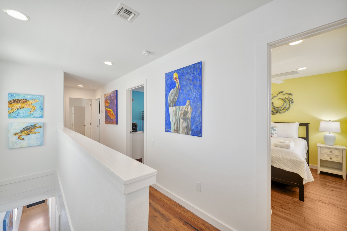Your upstairs hallway showcases vibrant coastal artwork, connecting beautifully appointed bedrooms in this bright, modern home.