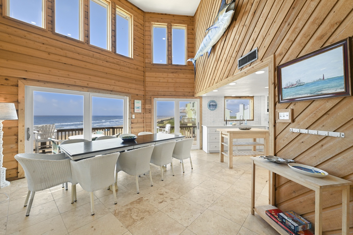 Light-filled living and dining space with soaring cathedral ceilings, natural wood warmth, and stunning ocean views through expansive windows framing your coastal retreat.