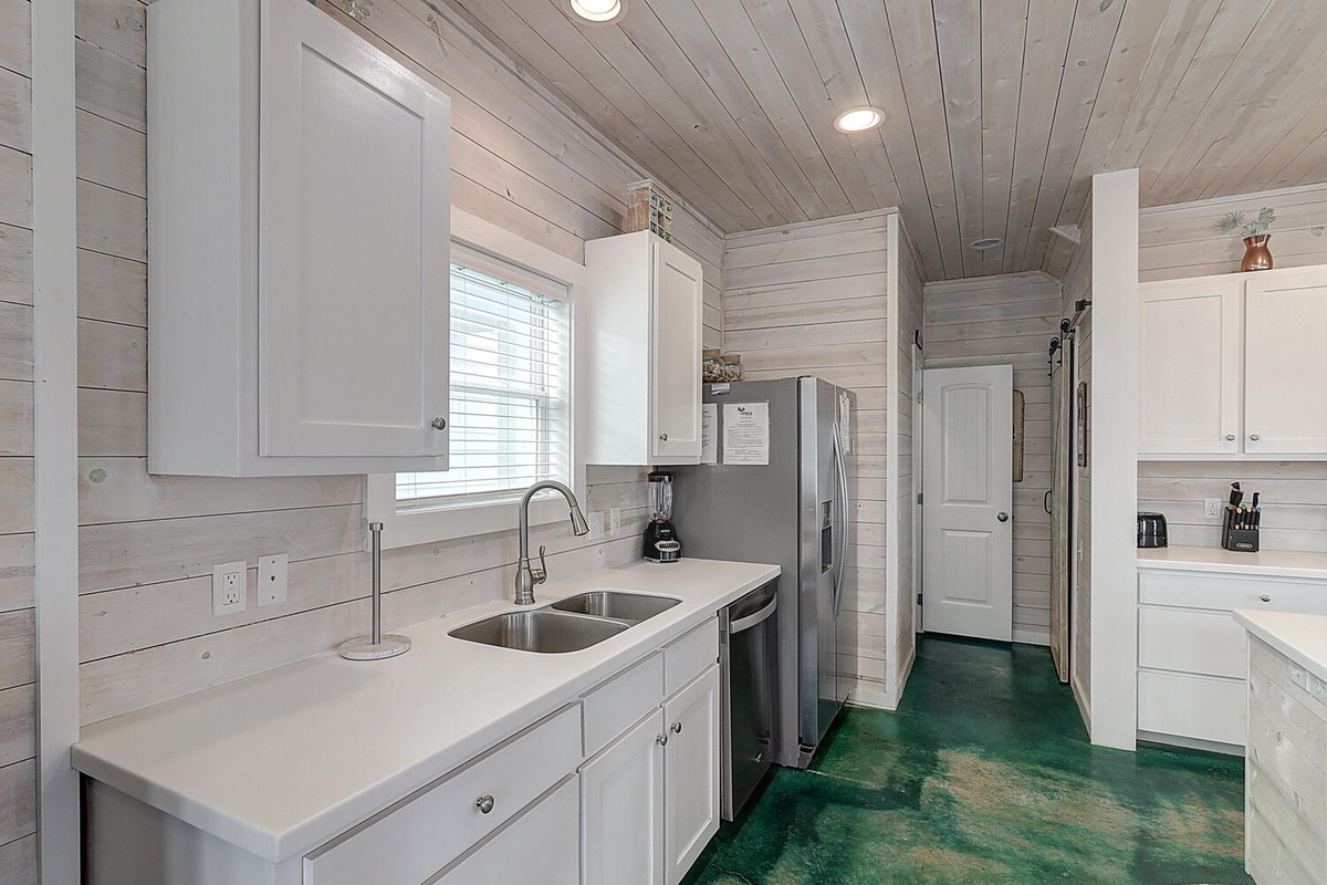Your fully equipped kitchen features modern appliances and coastal charm with weathered wood walls and a unique turquoise floor.