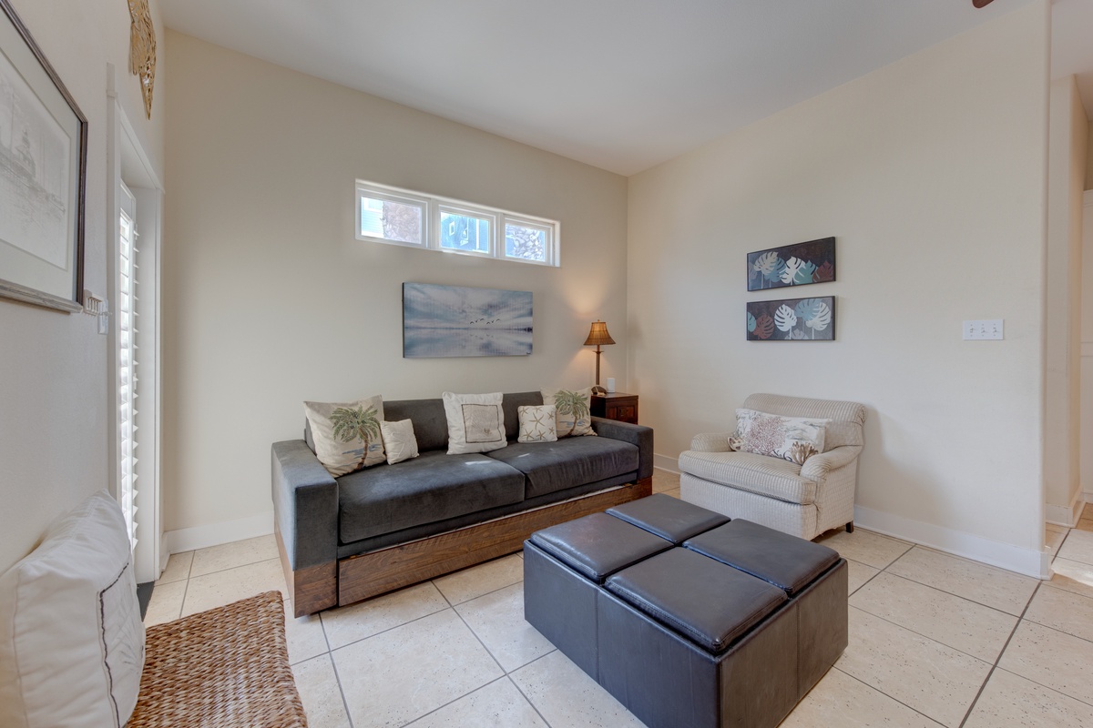 Sink into this serene living space where natural light floods through clerestory windows, illuminating your comfortable seating and coastal artwork.