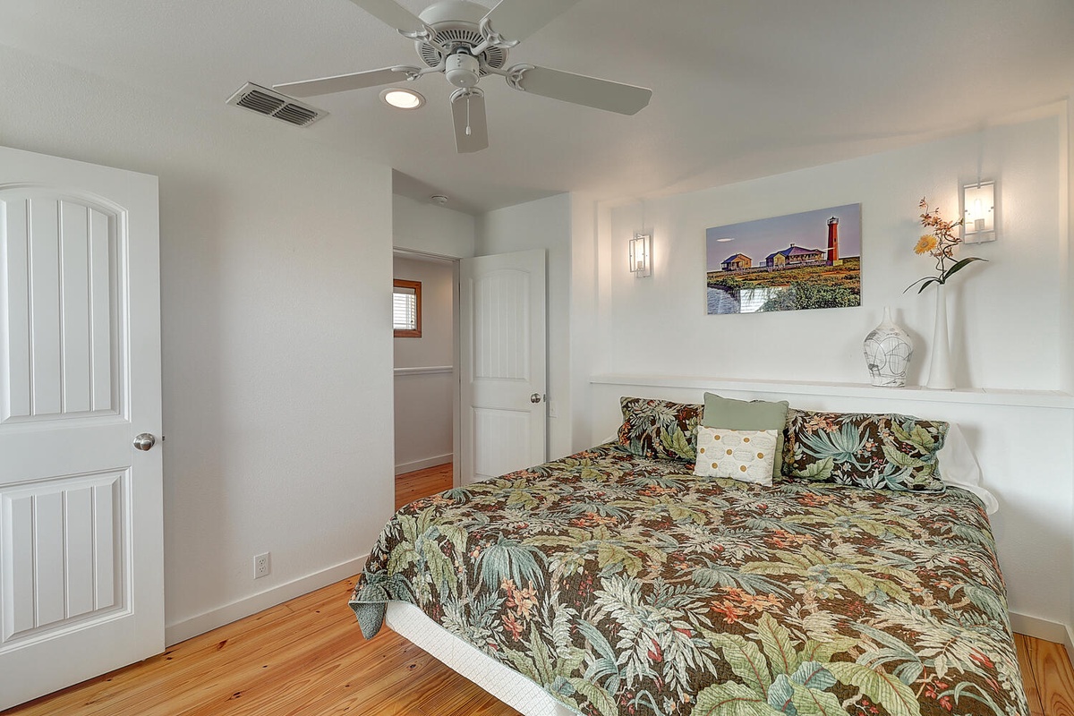 Rest comfortably in your coastal-themed bedroom with tropical bedding, ceiling fan, and charming lighthouse artwork creating a peaceful seaside retreat.