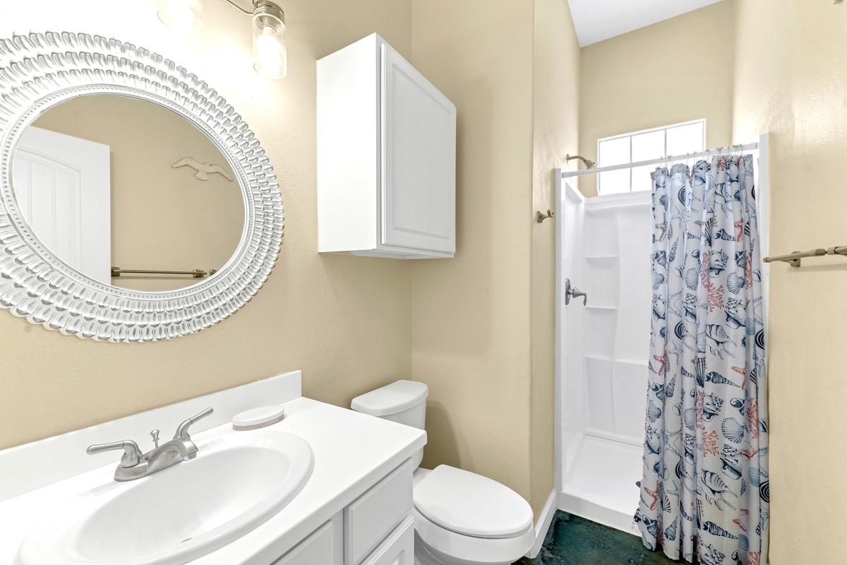Freshen up in your bright, well-appointed bathroom featuring a decorative mirror and colorful shower curtain for coastal charm.
