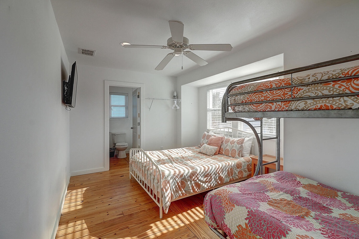 Your bright bedroom features a bunk bed and full bed with colorful bedding, ceiling fan, and natural light streaming across warm wood floors.