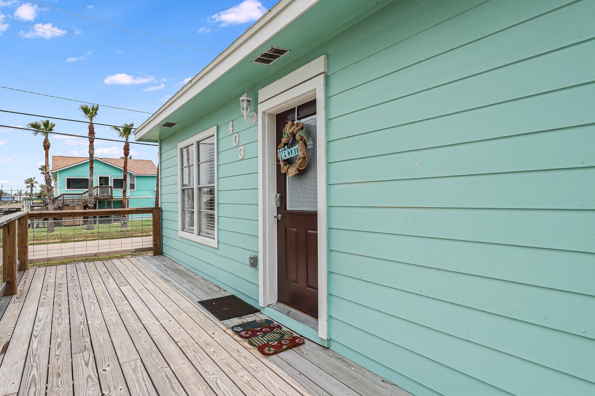 Charming turquoise beach cottage with welcome wreath creates a warm coastal arrival experience with palm trees and ocean-breeze setting.