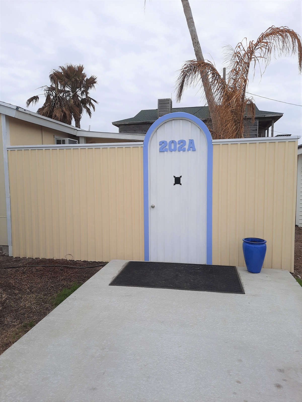 Find your private entrance at 202A, featuring distinctive blue accents and tropical landscaping in a quiet residential neighborhood.