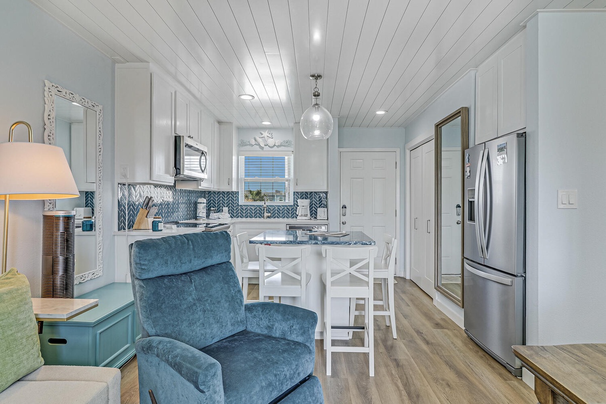Relax in your bright open-plan space featuring a fully equipped kitchen with coastal blue tilework and comfortable seating.