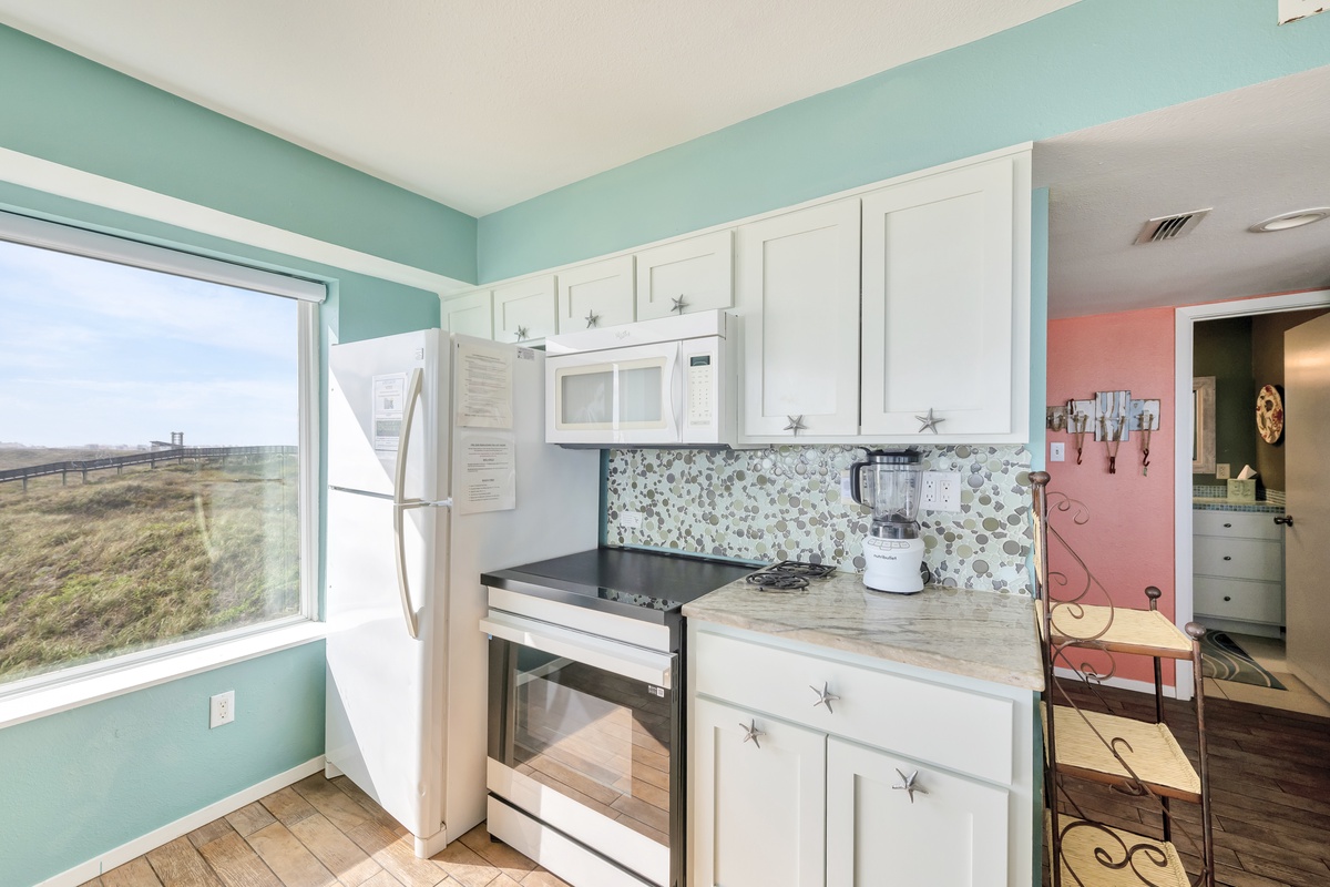 Your fully equipped kitchen features coastal charm with starfish-adorned cabinets and stunning natural views through the large window.