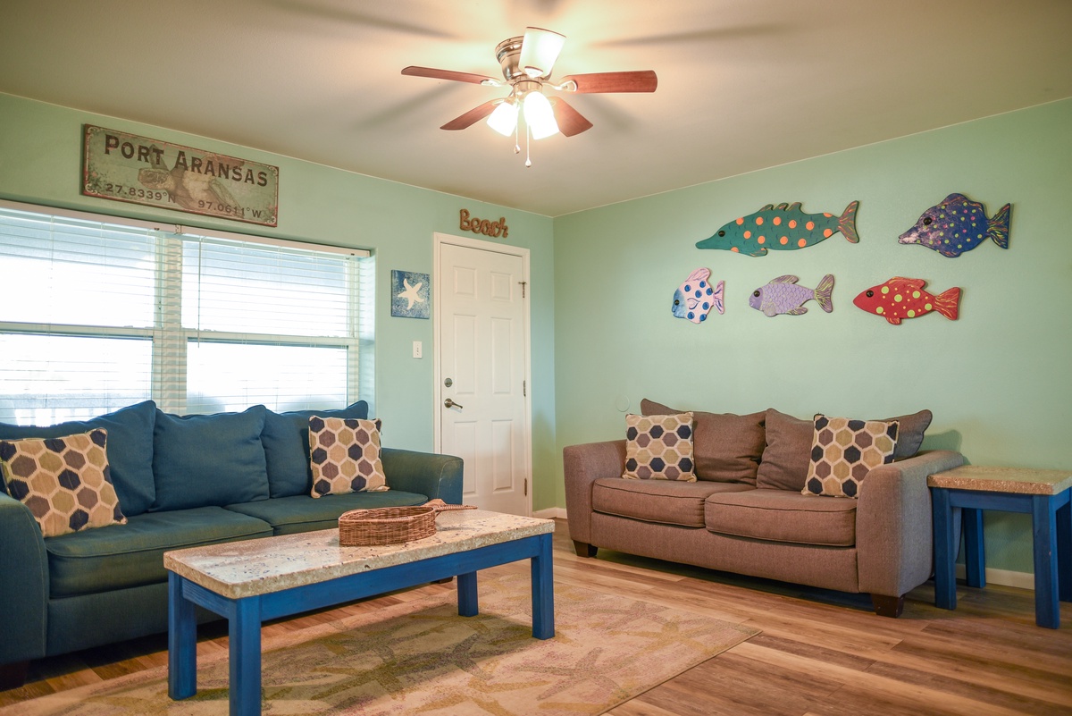 Unwind in your coastal-themed living room with comfy sofas, whimsical fish art, and cheerful beach vibes perfect for relaxing after adventures.