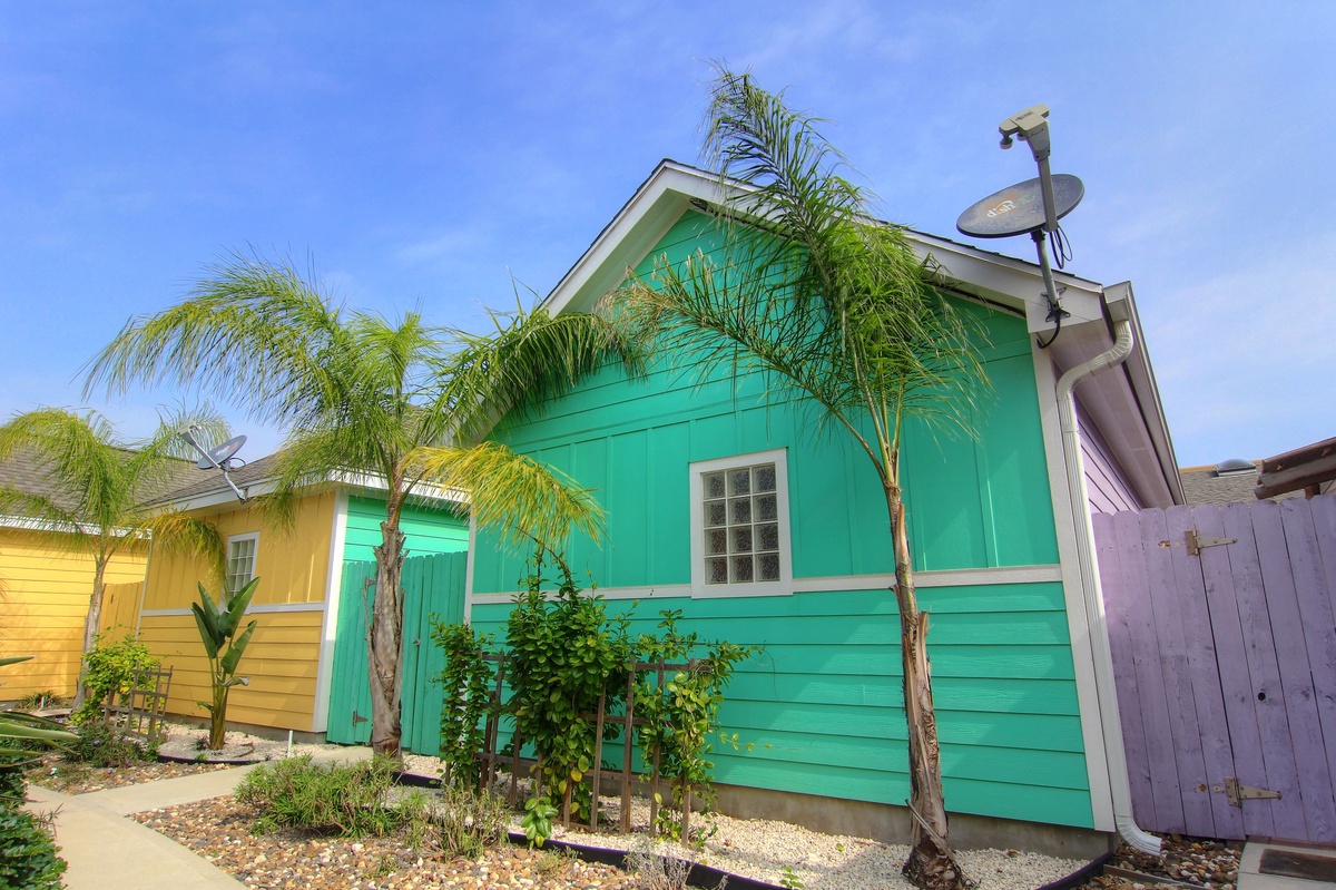 Colorful beachside cottages create a vibrant tropical neighborhood setting with lush palm trees and cheerful island architecture.