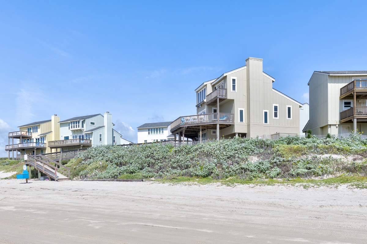Beachfront vacation homes situated along sandy shores with dune vegetation, offering direct beach access and coastal living in a serene setting.
