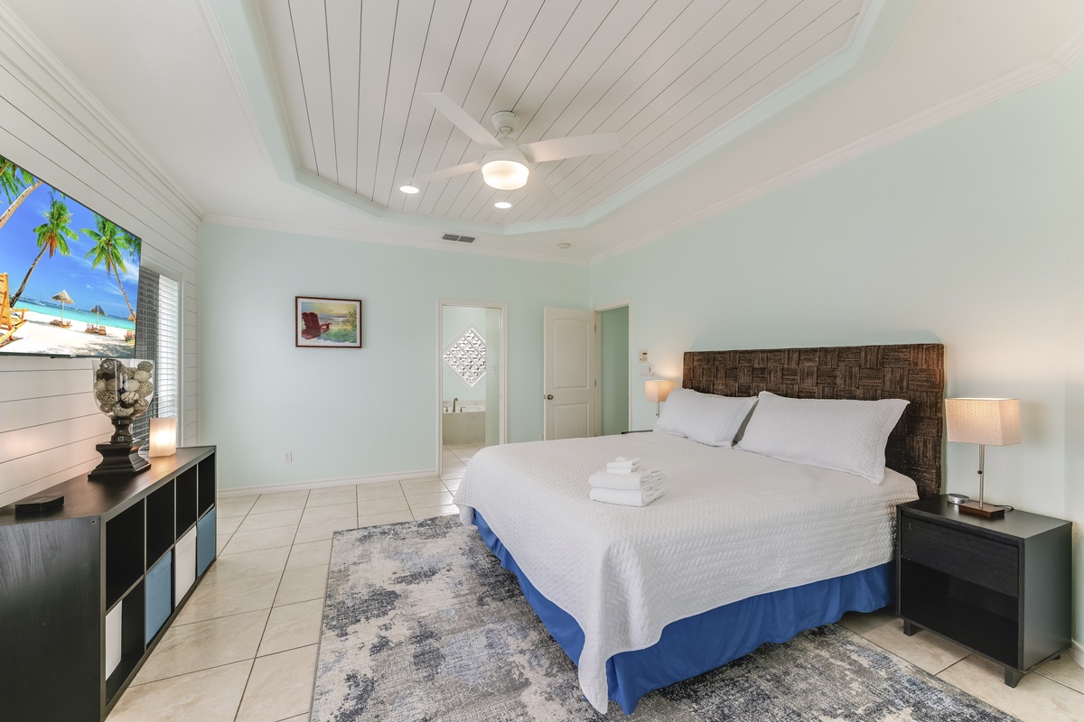 Unwind in this serene bedroom featuring a plush king bed with crisp linens, tropical ceiling fan, and calming coastal vibes.