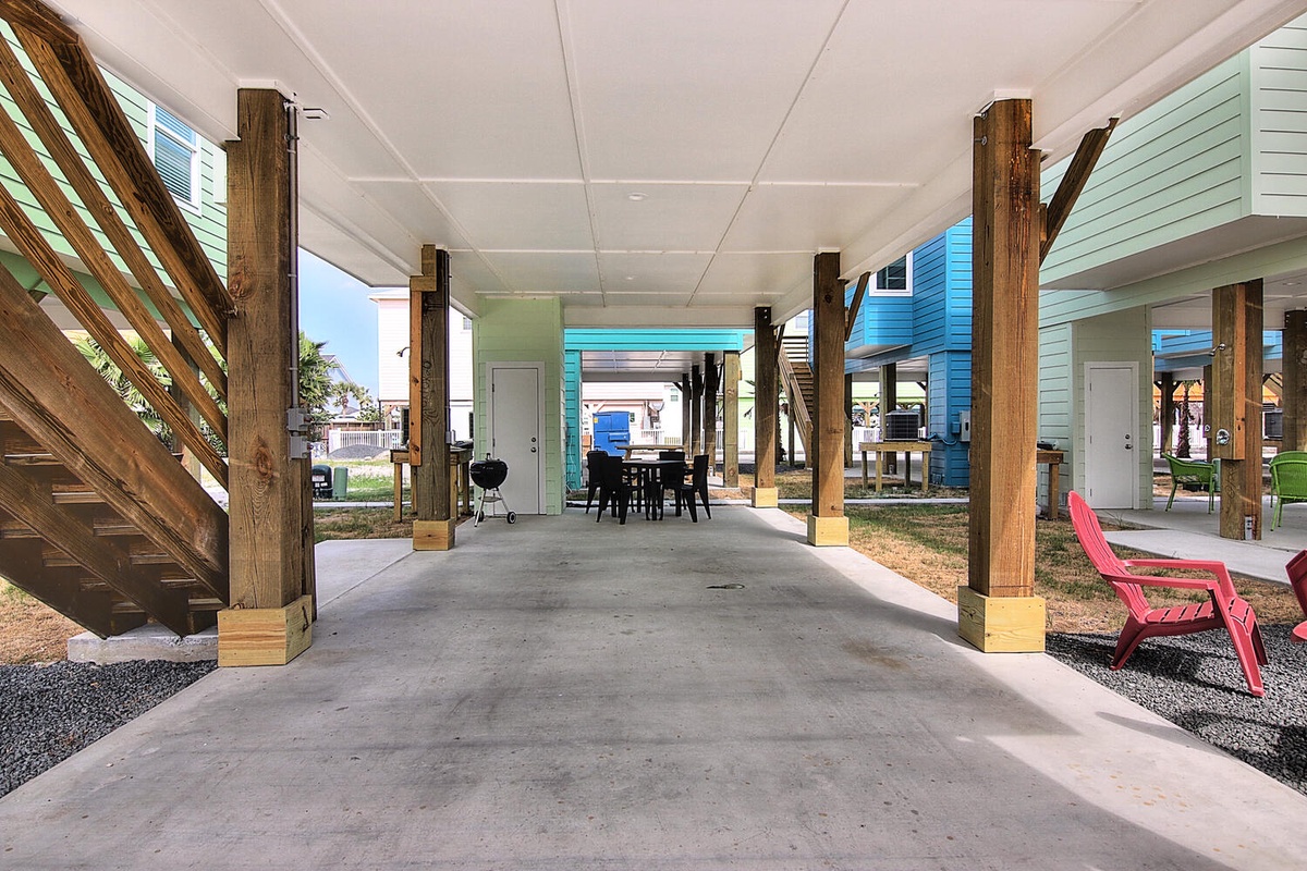 Spacious covered parking area beneath colorful beach houses with outdoor dining space and barbecue facilities for your coastal getaway.