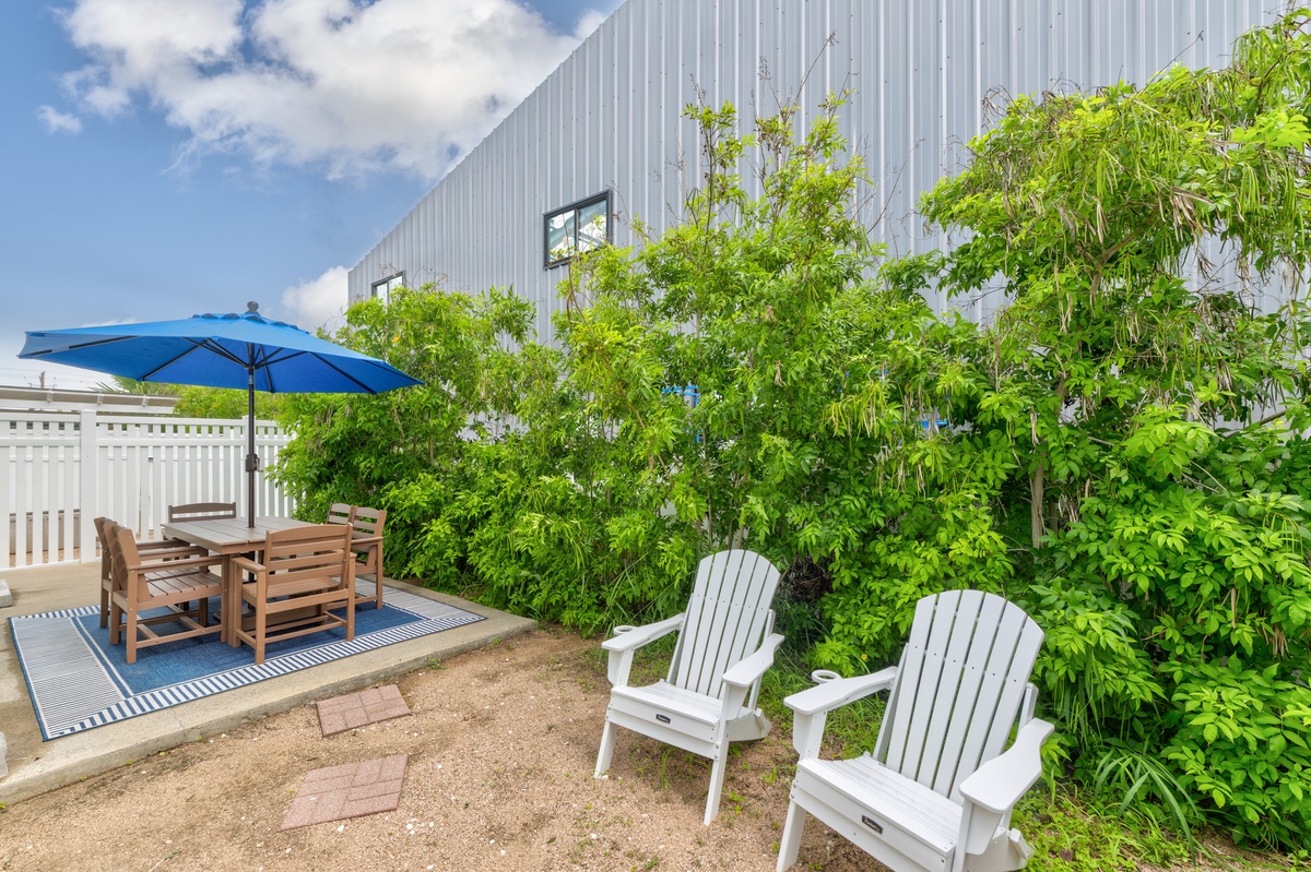 Relax in your private outdoor oasis with comfortable Adirondack chairs and dining space, surrounded by lush greenery under endless blue skies.