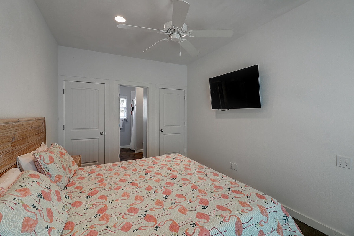 Your bright bedroom features a cozy floral bedspread, wall-mounted TV, and ceiling fan for perfect comfort during your stay.