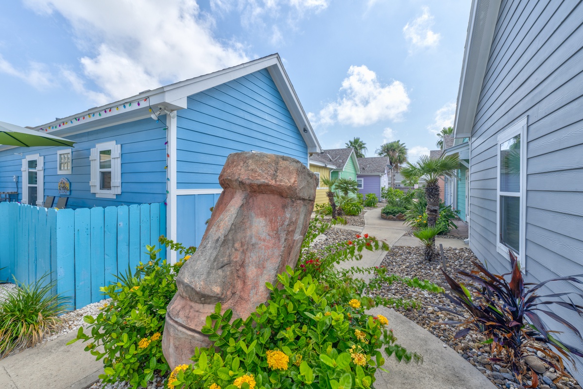 Charming coastal village features colorful beach houses and tropical landscaping with distinctive stone sculpture centerpiece.