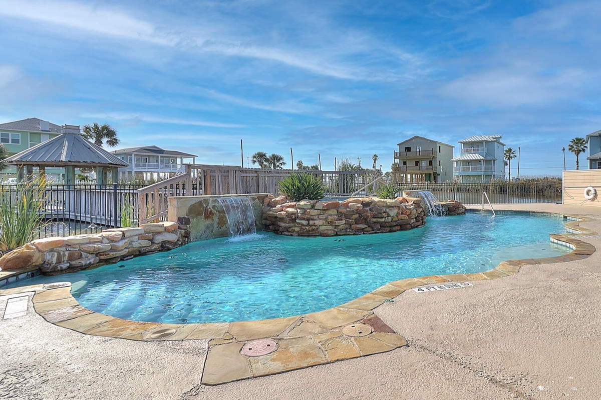 Resort-style pool with waterfall features and stone accents creates a tropical oasis surrounded by coastal vacation homes.