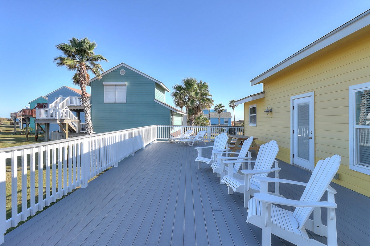 Your spacious deck offers the perfect spot to unwind with comfortable Adirondack chairs overlooking tropical palms and colorful beach houses.