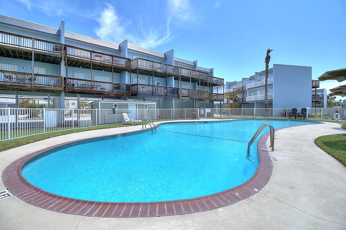 Sparkling pool area surrounded by coastal architecture and balconies under a brilliant blue sky.