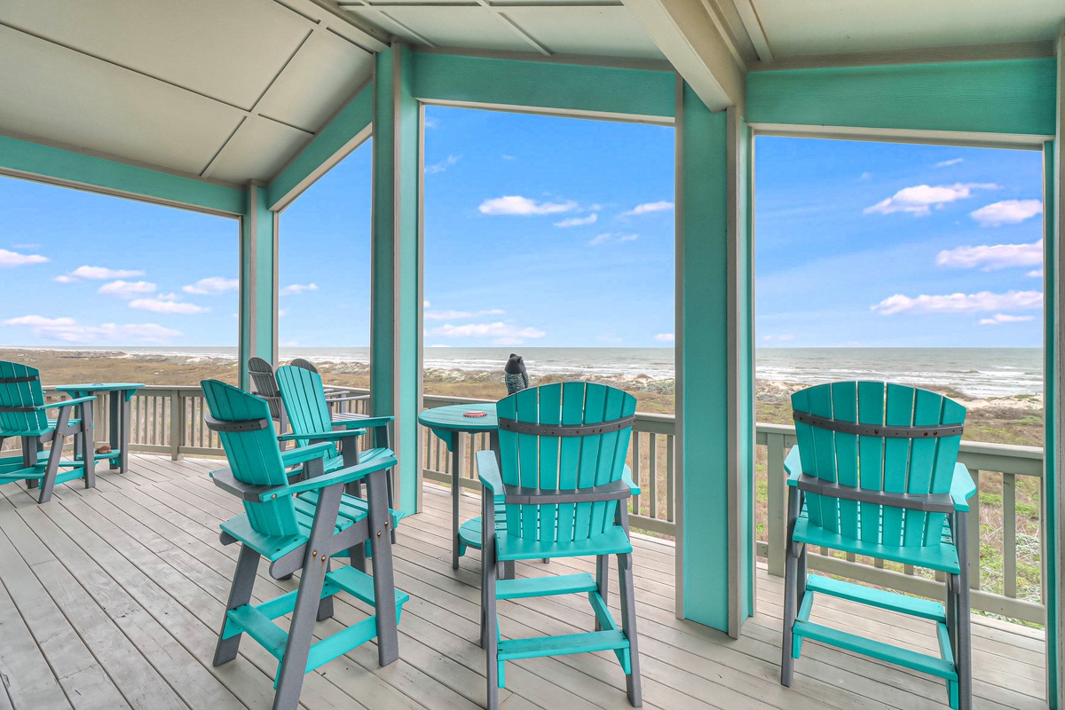 Relax in these cozy turquoise chairs while soaking in stunning ocean views through floor-to-ceiling windows on your private covered deck.