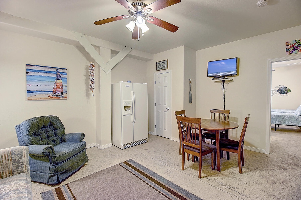 Relax in your cozy open-plan living space with comfortable seating, dining table, and beach-themed decor creating a welcoming coastal atmosphere.