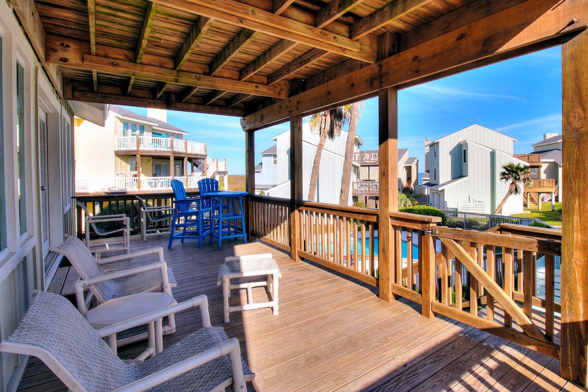 Your covered deck offers comfortable seating with blue bar chairs and lounge furniture, perfect for relaxing while enjoying coastal neighborhood views.