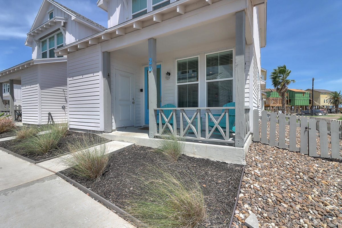 Charming coastal cottage with turquoise accents and covered front porch, featuring modern beach house architecture in a sunny seaside neighborhood.