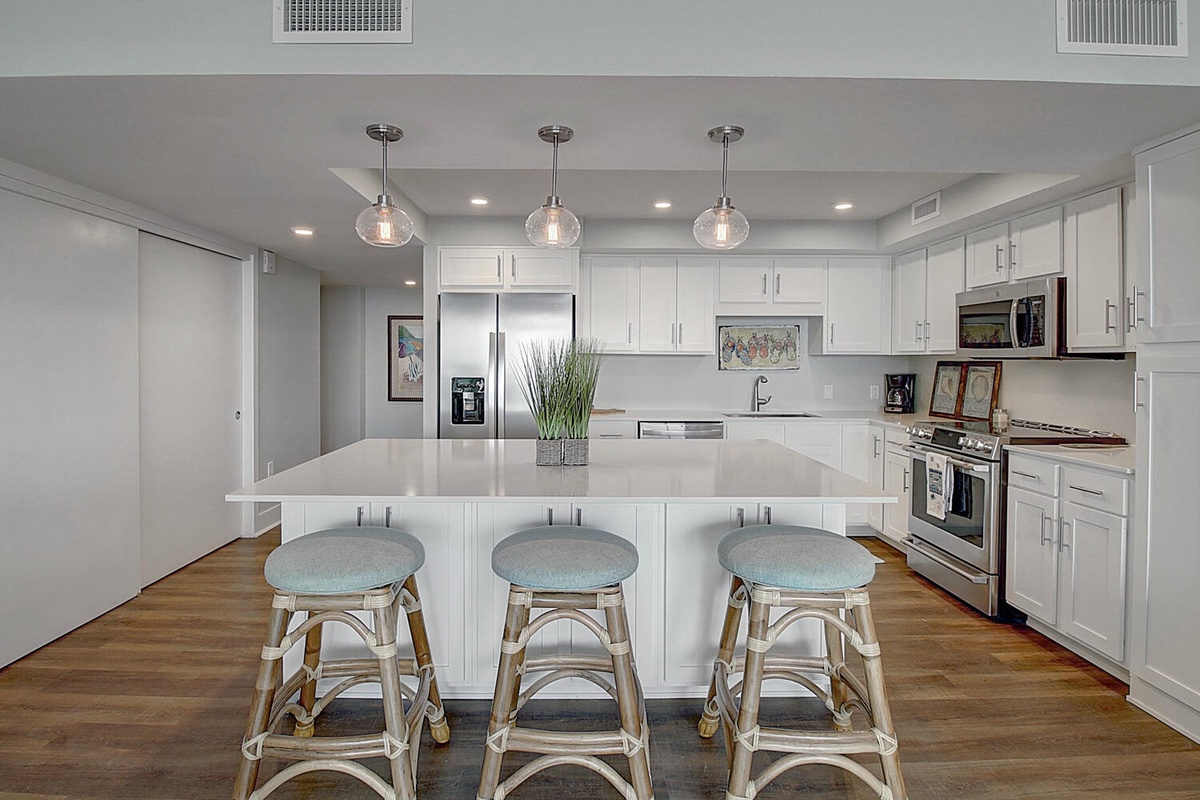 Your sleek kitchen features pristine white cabinets, gleaming countertops, and modern pendant lighting—perfect for preparing memorable meals during your stay.