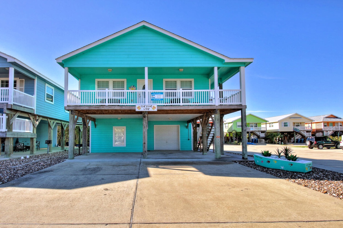 Charming turquoise beach house with covered parking and coastal neighborhood setting featuring colorful stilt homes.