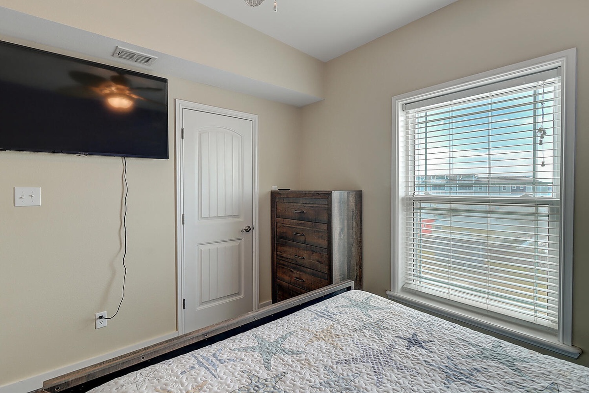 Unwind in your cozy bedroom featuring a wall-mounted TV, rustic dresser, and large windows that fill the space with natural light.
