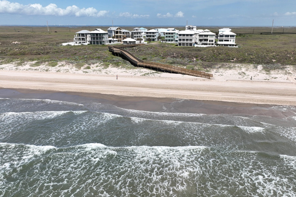 Aerial view of beachfront vacation rentals with private boardwalk access to pristine sandy shores and rolling ocean waves.
