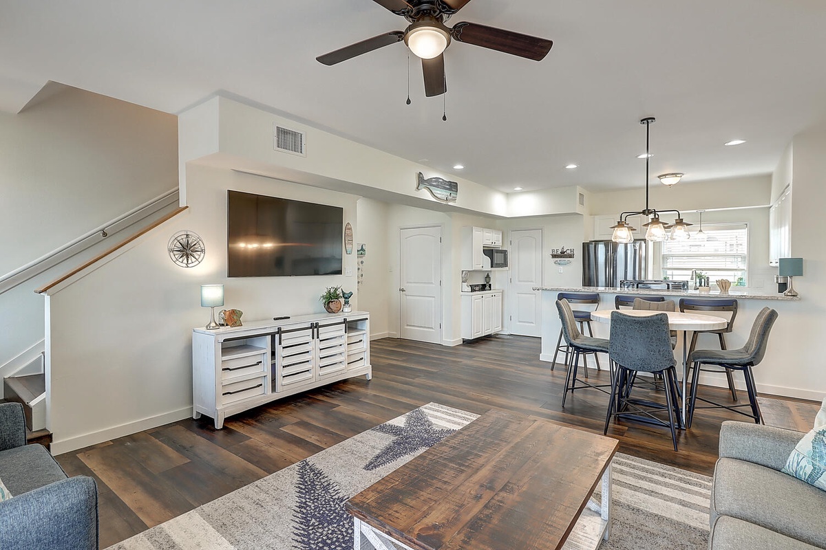 Relax in your spacious open-concept living area with modern furnishings, ceiling fan, and seamless flow to the fully-equipped kitchen.