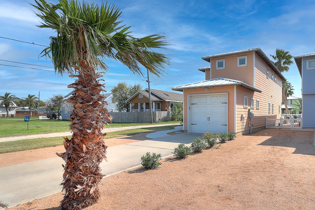 Charming coastal property with warm coral exterior, private garage, and mature palm tree creating a welcoming tropical arrival experience.