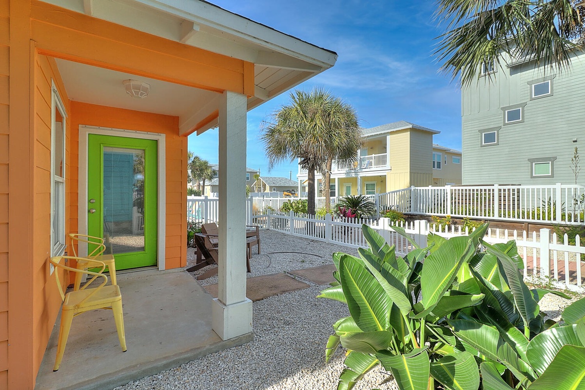 Bright orange cottage with vibrant green door sits among tropical palms and colorful neighboring homes in this cheerful coastal community.