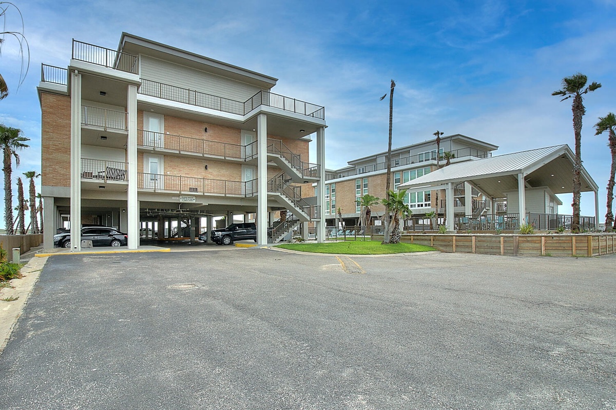 Multi-story beachside property featuring convenient ground-level parking and tropical palm landscaping in a coastal residential area.