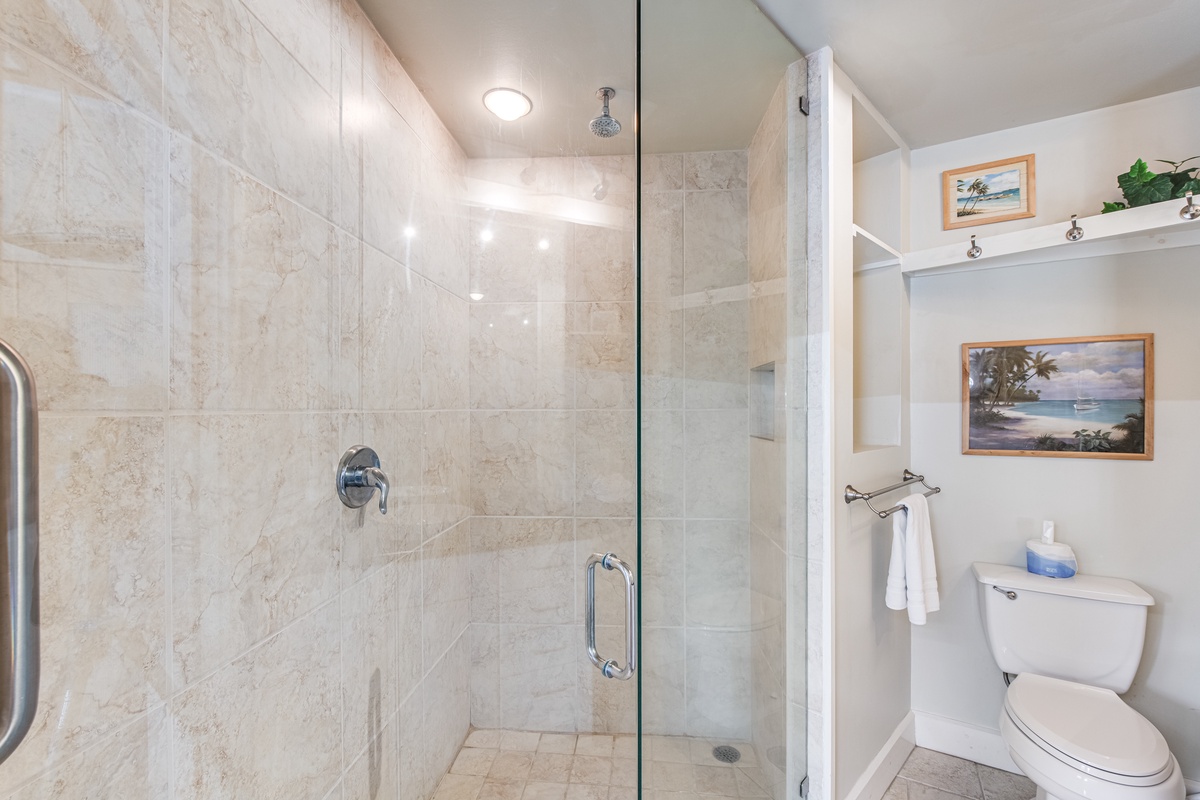 Step into your spa-like bathroom featuring a spacious glass-enclosed shower with marble tiles and tropical artwork to inspire relaxation.