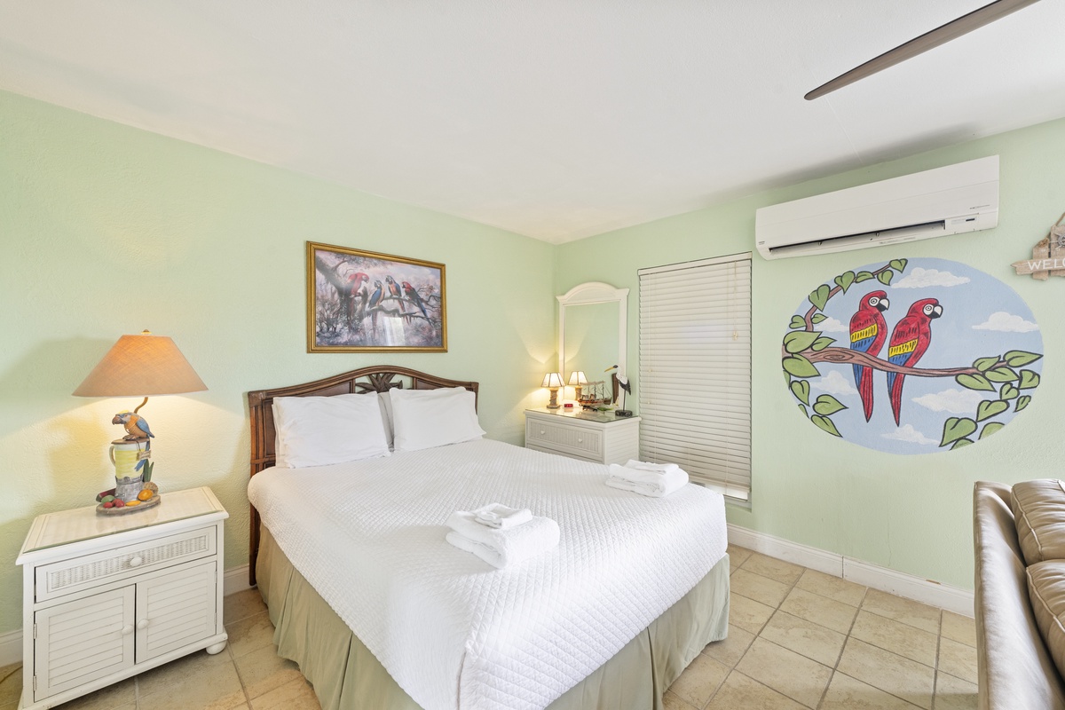 Your tropical bedroom sanctuary features crisp linens, playful parrot artwork, and cool air conditioning for perfect island comfort.