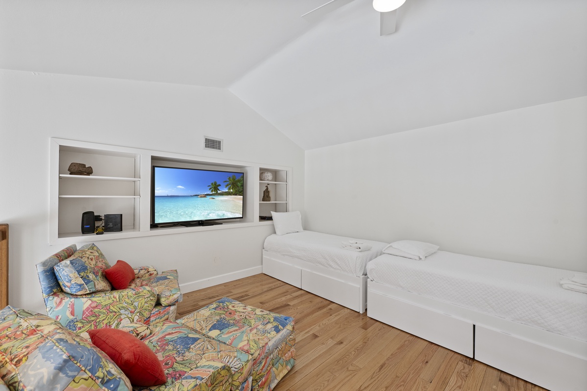 Relax in your bright bedroom featuring twin beds, built-in entertainment center, and tropical beach scenes on the large TV.