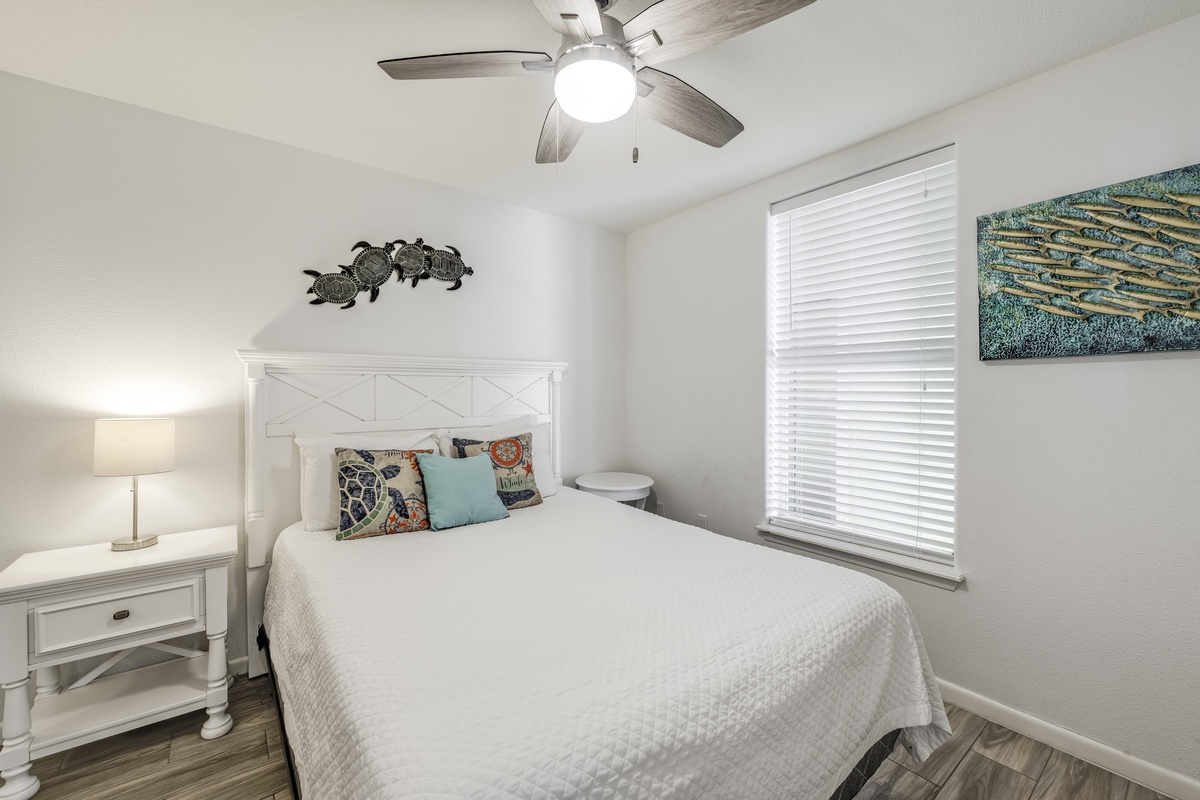 Your coastal-inspired retreat awaits with crisp linens and beachy decor. Drift off under the gentle ceiling fan as natural light filters through, creating your perfect vacation sanctuary.