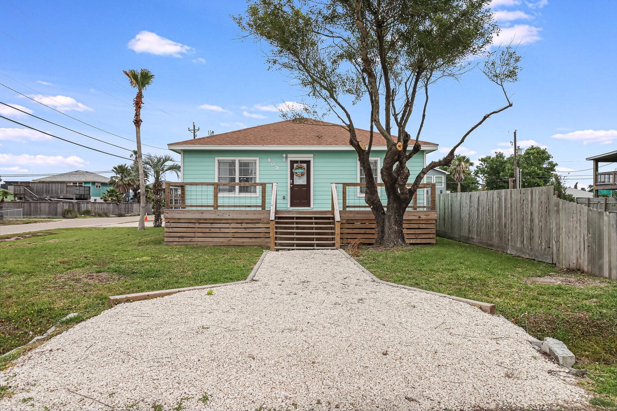Charming mint-green cottage with welcoming front porch and mature shade tree in peaceful residential neighborhood.