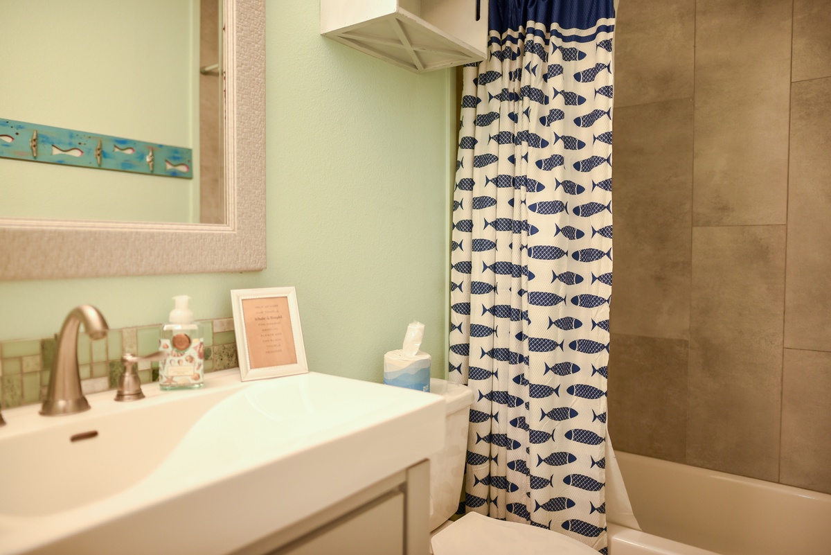 Step into your charming bathroom with coastal-inspired fish shower curtain, modern vanity, and thoughtful amenities ready for your refreshing stay.