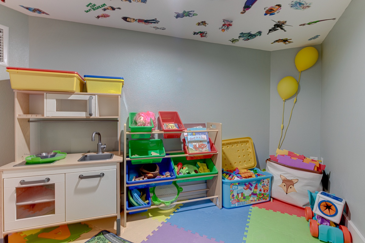 Your little ones will love this cheerful playroom with toy kitchen, colorful storage, and fun ceiling decals for imaginative adventures.