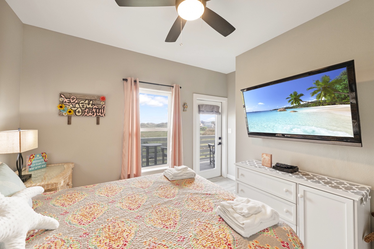Your serene bedroom features a comfortable bed, large TV, and balcony access with scenic views for the perfect retreat.