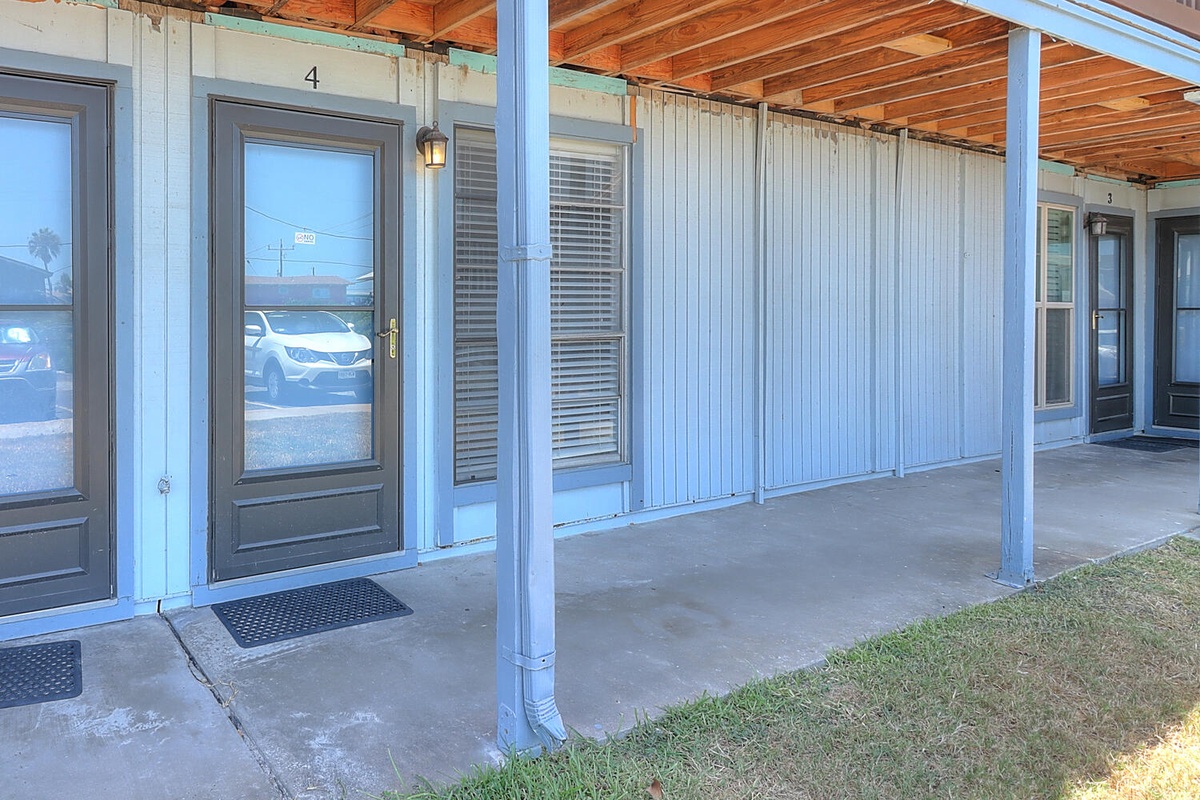 Clean exterior walkway with covered porch area and parking visible nearby for convenient access.